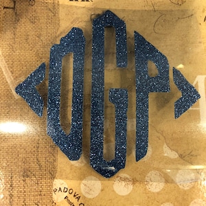 May include: A blue glitter monogram with the letters "OGP" in a diamond shape.