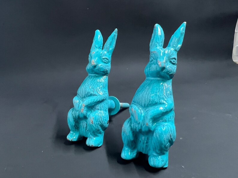 May include: Two turquoise blue ceramic bunny rabbit figurines. The bunnies are sitting with their paws crossed and have a distressed finish.