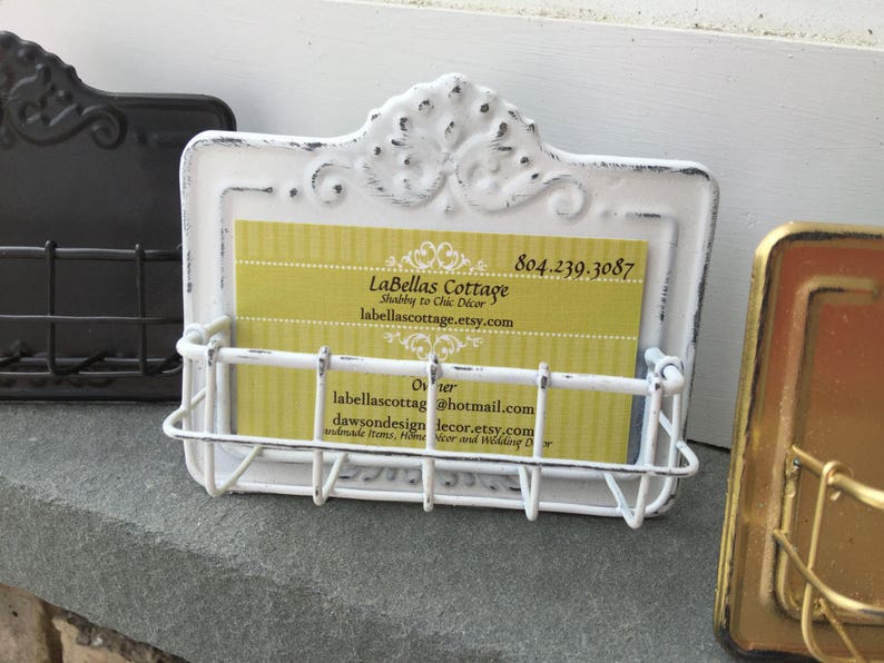 May include: White metal business card holder with a distressed finish and ornate design. The holder has a wire rack to hold business cards. The business card inside the holder reads "LaBellas Cottage, Shabby to Chic D&eacute;cor, labellascottage.etsy.com, 804.239.3087, Owner, labellascottag@hotmail.com, dawsondesigndecor.etsy.com, Handmade Items, Home D&eacute;cor and Wedding D&eacute;cor."