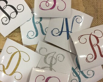 May include: Assortment of glitter monogram decals in various colours, including gold, silver, pink, blue, and teal. Each decal features a single letter in a cursive font.