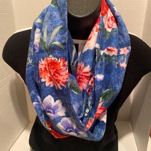 Puede incluir: Una bufanda infinita azul con estampado floral con flores rojas, rosas, blancas y verdes. La bufanda está hecha de una tela suave y cómoda y es perfecta para agregar un toque de estilo a cualquier atuendo.