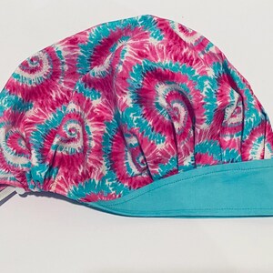 Könnte beinhalten: Eine rosa-blaue Batik-Kochmütze mit einem türkisfarbenen Rand. Die Mütze hat einen Kordelverschluss.