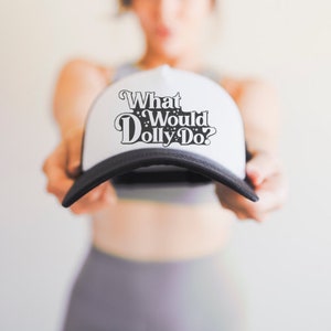 May include: White trucker hat with black mesh back and black text that reads "What Would Dolly Do?"