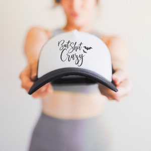 May include: White and black trucker hat with the text "Bat Shit Crazy" in black script font and two black bats on the front.