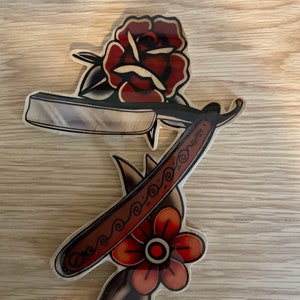 May include: A wooden cutout of a traditional tattoo design featuring a red rose and a straight razor with a decorative handle.