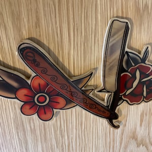 May include: A wooden cutout of a vintage straight razor with a rose and a flower, all in shades of red, brown, and white.