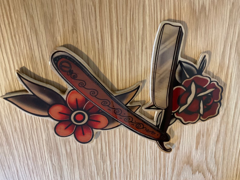 May include: A wooden cutout of a vintage straight razor with a rose and a flower, all in shades of red, brown, and white.