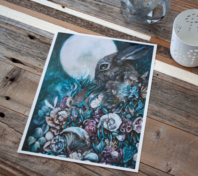 May include: A watercolor painting of a rabbit in a forest setting. The rabbit is brown and white and is surrounded by lush green foliage and flowers. The moon is visible in the background, shining a soft light on the scene.