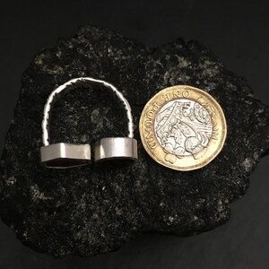 May include: A silver ring with two red gemstone settings. The ring is shown next to a British one pound coin for size comparison.