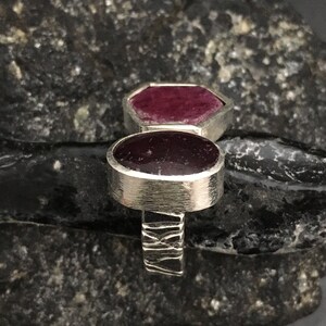 May include: A silver ring with two deep red ruby stones. The ring has a textured band.