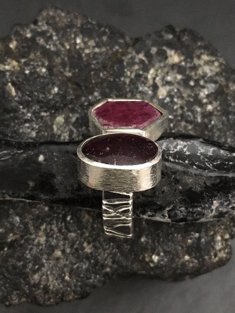 May include: A silver ring with two deep red ruby stones. The ring has a textured band.