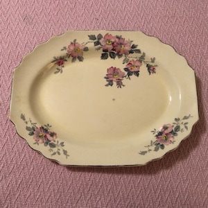 May include: A white oval serving dish with a floral design. The dish has a scalloped edge and features pink and green flowers.