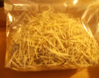 May include: A clear plastic bag filled with a large quantity of thin, pointed, light-colored porcupine quills. The quills are varying in length and thickness, featuring natural cream, yellow, and dark brown or black striped colorations throughout.
