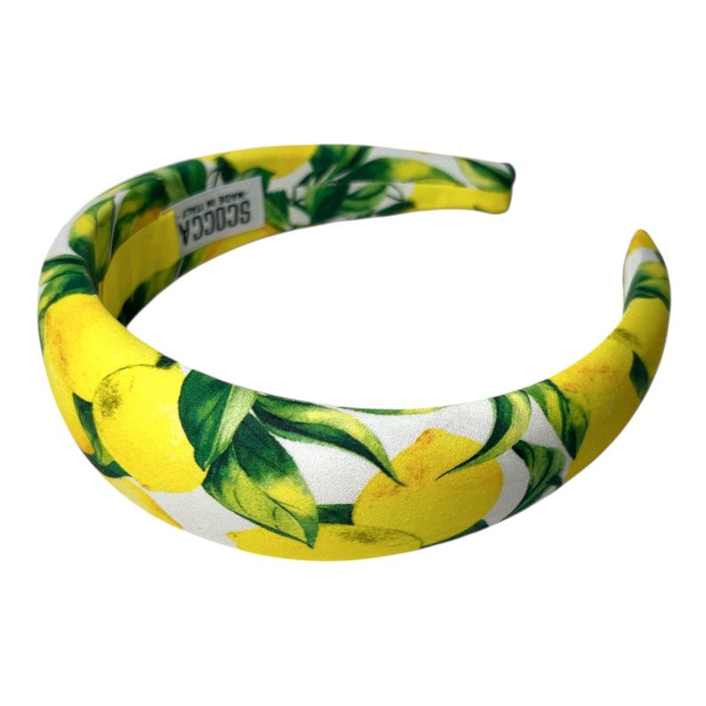 May include: A padded headband with a bright yellow and green lemon print. The headband is curved and has the text "SCOCCA MADE IN ITALY" printed on the inside.