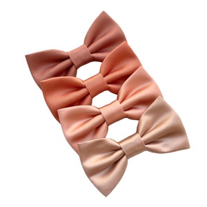 May include: Three satin bow ties in shades of peach, coral, and light pink.