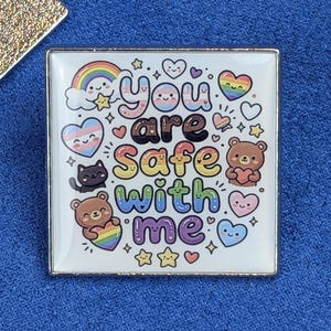 Peut inclure: Un pin's carré en émail avec le texte "you are safe with me" en lettres bulles colorées. Le motif comprend un arc-en-ciel, un chat noir, deux ours bruns tenant des cœurs, ainsi que divers petits cœurs et étoiles aux tons pastel et arc-en-ciel.