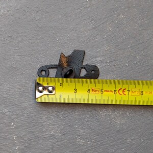 May include: A black metal decorative pin in the shape of a hat, with a pin back. The pin is approximately 1.5 inches long. A yellow Stanley measuring tape is next to the pin.