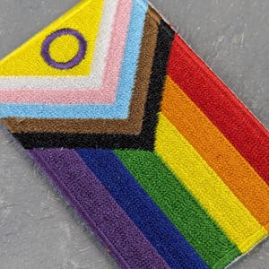 Peut inclure: Écusson brodé représentant le drapeau Progress Pride. Le design comprend les couleurs de l'arc-en-ciel, ainsi que des rayures représentant la communauté transgenre, les personnes de couleur et la communauté intersexe. L'écusson a une bordure violette.