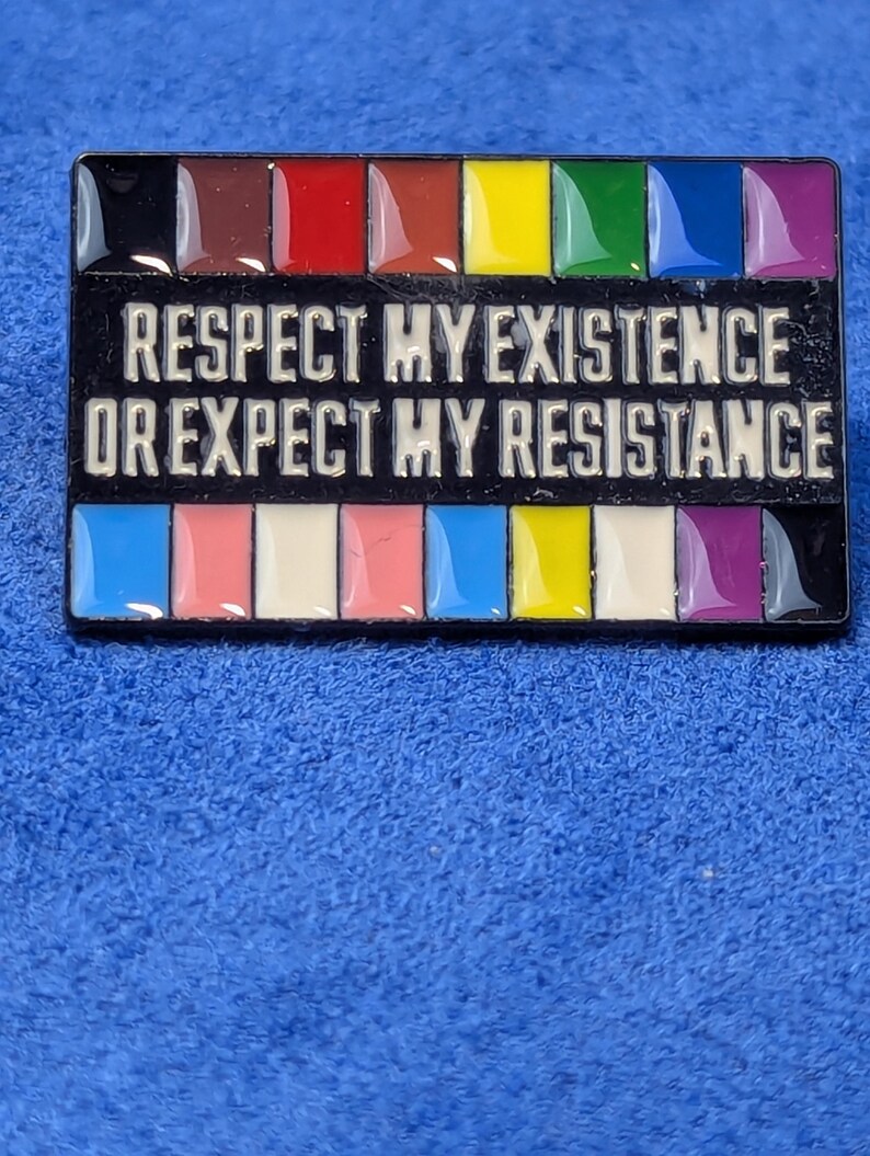 May include: A rectangular pin with a black background and the text "RESPECT MY EXISTENCE OR EXPECT MY RESISTANCE" in white. The pin features a rainbow of colors at the top and bottom, including brown, red, yellow, green, blue, and purple.