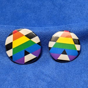 May include: Two circular buttons with a rainbow and black and white chequered design. The buttons display a rainbow of colours: red, orange, yellow, green, blue, and purple. The background is a solid blue.