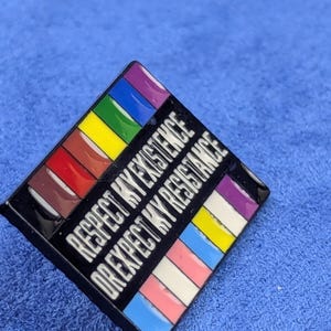 May include: A square enamel pin with a black border and the text "RESPECT MY EXISTENCE OR EXPECT MY RESISTANCE" in white. The pin features a rainbow design and other pride flag colors.
