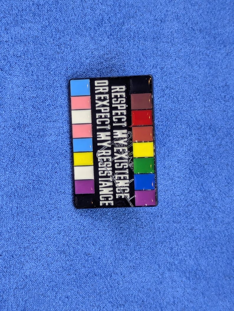 May include: A rectangular pin with a black border and a colorful design. The pin features the text "RESPECT MY EXISTENCE OR EXPECT MY RESISTANCE" in white. The design includes a series of colored blocks.