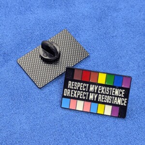 May include: A rectangular enamel pin with the text "RESPECT MY EXISTENCE OR EXPECT MY RESISTANCE" in white. The pin features a rainbow color scheme and a black backing with a pin clasp.