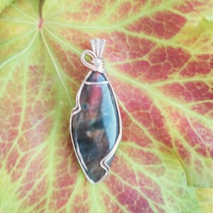 May include: A silver wire wrapped pendant featuring a dark green, brown, and red gemstone with a unique, irregular shape.