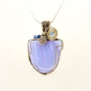 May include: A silver wire wrapped pendant featuring a light purple agate stone with blue accents. The pendant is attached to a silver chain.