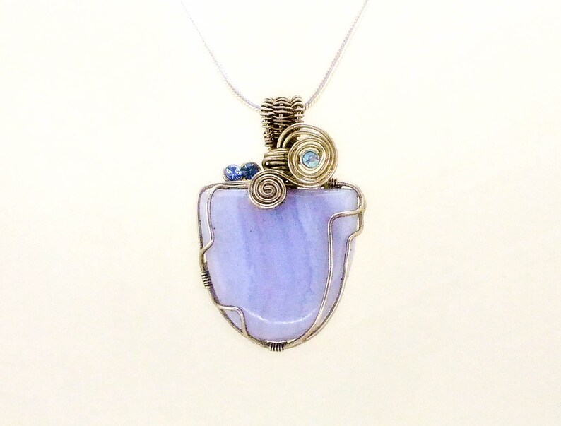 May include: A silver wire wrapped pendant featuring a light purple agate stone with blue accents. The pendant is attached to a silver chain.