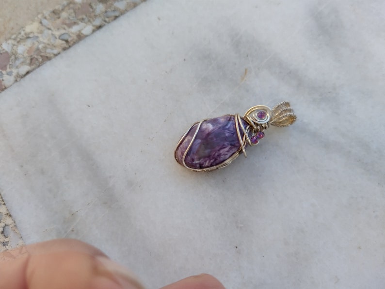 May include: A purple and silver wire-wrapped pendant with small pink gemstones.