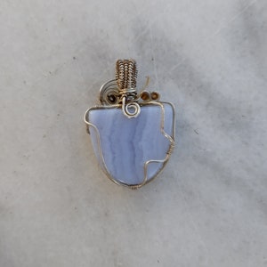 May include: A blue agate pendant wrapped in silver wire with a gold wire loop at the top.