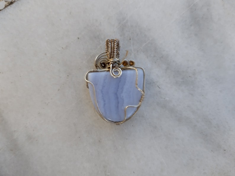 May include: A blue agate pendant wrapped in silver wire with a gold wire loop at the top.