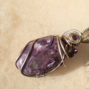 May include: A purple and silver wire-wrapped pendant featuring a natural stone with a swirling pattern. The pendant is accented with small purple beads.