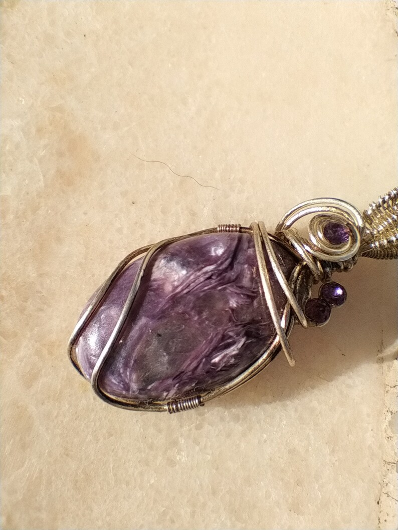 May include: A purple and silver wire-wrapped pendant featuring a natural stone with a swirling pattern. The pendant is accented with small purple beads.