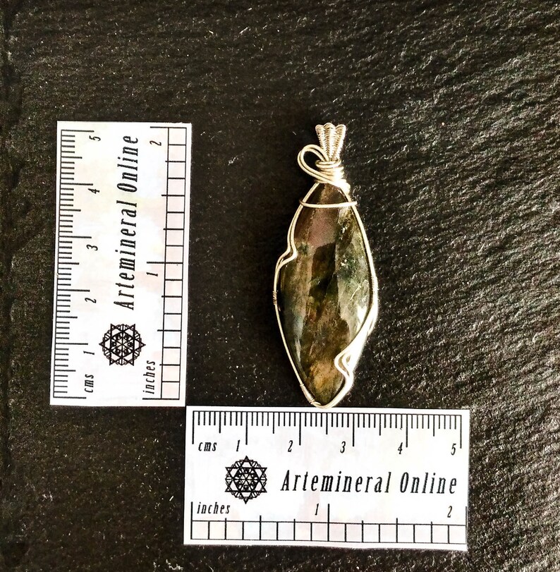May include: A silver wire wrapped pendant featuring a dark green and black labradorite gemstone. The pendant is approximately 2 inches long.