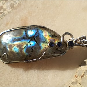 May include: A silver wire wrapped pendant featuring a large iridescent labradorite gemstone with two smaller blue sapphire accents.