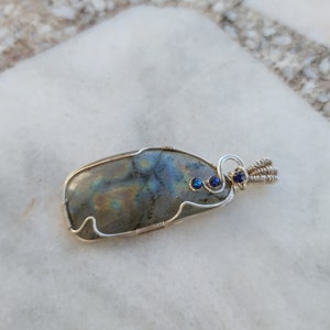 May include: A silver wire wrapped pendant featuring a large iridescent labradorite gemstone with two small blue accent stones.