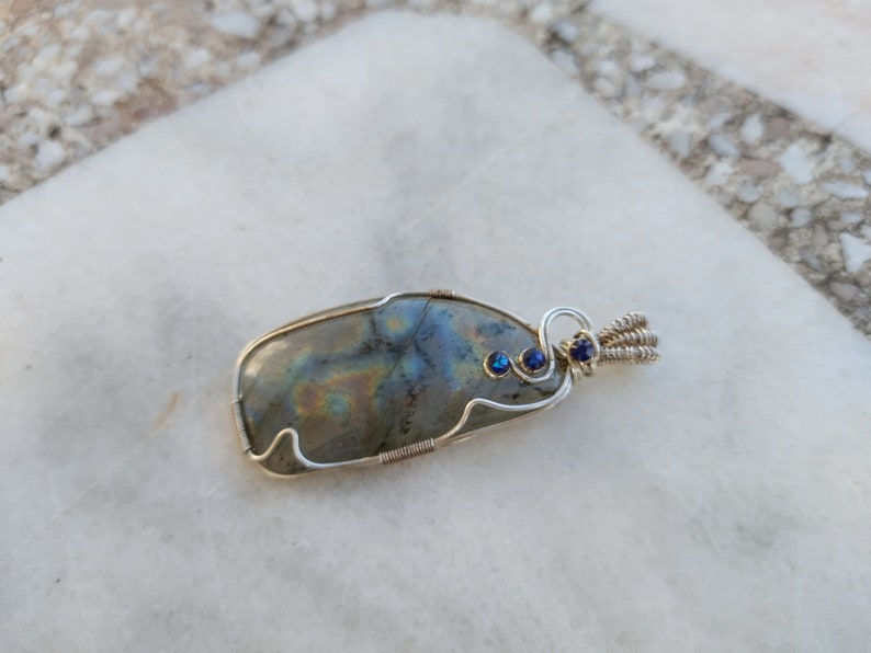 May include: A silver wire wrapped pendant featuring a large iridescent labradorite gemstone with two small blue accent stones.