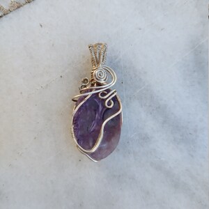 May include: A purple amethyst stone wrapped in silver wire, forming a pendant.