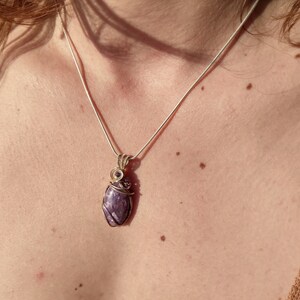 May include: A silver chain necklace with a purple gemstone pendant wrapped in gold wire.