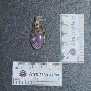 May include: Purple amethyst gemstone wrapped in gold wire with two small pink gemstones at the top, forming a pendant. The pendant is approximately 2 inches long.