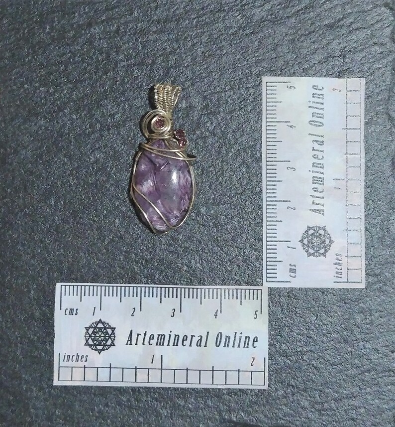May include: Purple amethyst gemstone wrapped in gold wire with two small pink gemstones at the top, forming a pendant. The pendant is approximately 2 inches long.