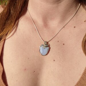May include: A silver chain necklace with a pendant featuring a light blue agate stone wrapped in silver wire and accented with small blue and clear gemstones.