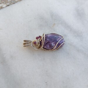 May include: A purple and silver wire-wrapped pendant with small red gemstones.