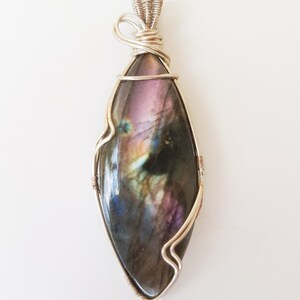May include: A silver wire wrapped pendant featuring a large iridescent labradorite gemstone with shades of purple, blue, and green.