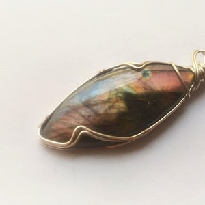 May include: A silver wire wrapped pendant featuring a large, iridescent labradorite gemstone with shades of green, brown, and pink.