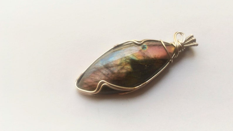 May include: A silver wire wrapped pendant featuring a large, iridescent labradorite gemstone with shades of green, brown, and pink.
