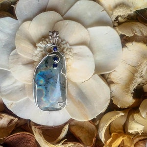 May include: A silver wire wrapped pendant featuring a blue-green iridescent gemstone with three small blue accent stones.