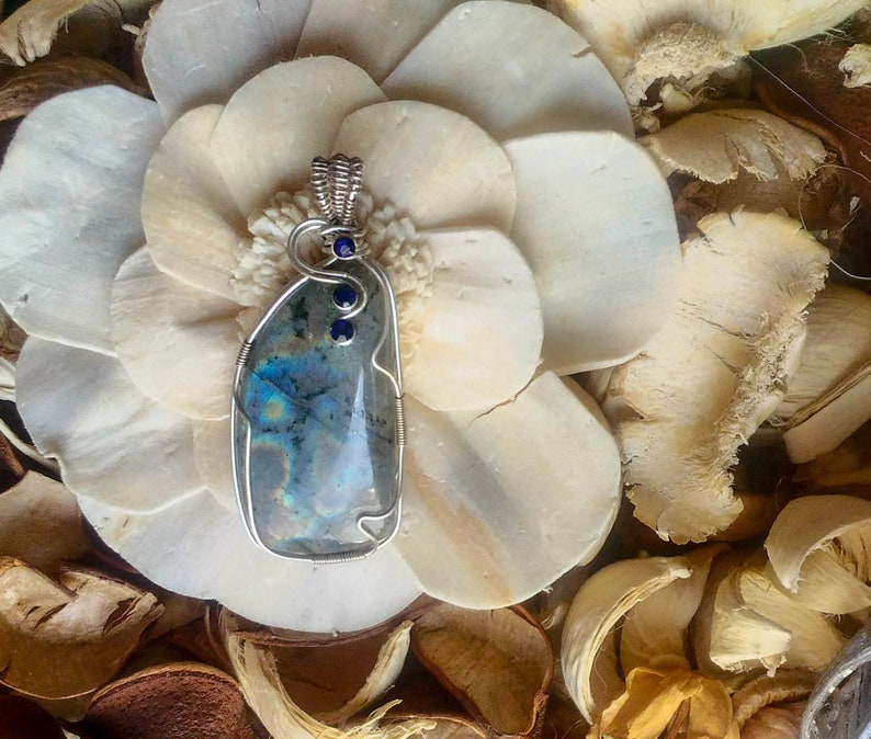 May include: A silver wire wrapped pendant featuring a blue-green iridescent gemstone with three small blue accent stones.